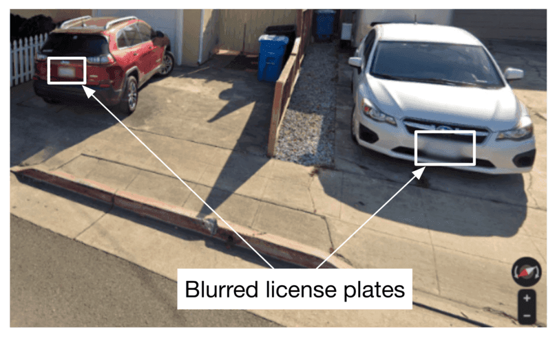 Image represents a street-level view of a residential driveway with two cars parked.  A red SUV is parked on the left, and a white sedan is parked on the right.  Both license plates are rectangular areas that have been intentionally blurred, indicated by white rectangular boxes overlaid on the image.  White arrows point from these blurred license plate boxes to the text 'Blurred license plates' located at the bottom center of the image.  The driveway is made of concrete, and a section of curb and a metal beam are visible in the foreground.  A portion of a white picket fence is visible in the upper left corner, and a blue recycling bin is partially visible behind the white car.  In the bottom right corner, there's a small compass-like icon and plus/minus buttons, suggesting the image is from a map application or similar platform allowing for zoom functionality.